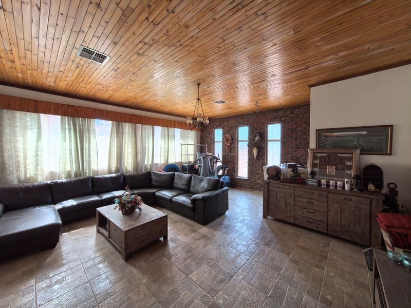 Spacious living room featuring a distinctive timber tongue and groove ceiling, exposed brick feature wall, and durable tiled flooring.