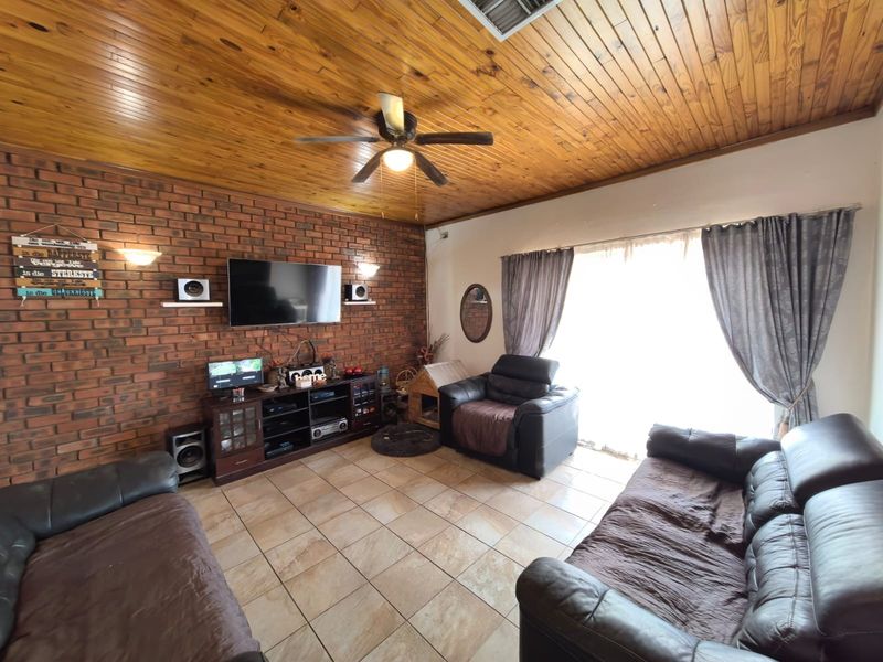 Living room featuring an exposed brick feature wall, timber ceiling, ceiling fan, and ceramic tiled flooring with access to the outdoors via sliding doors.