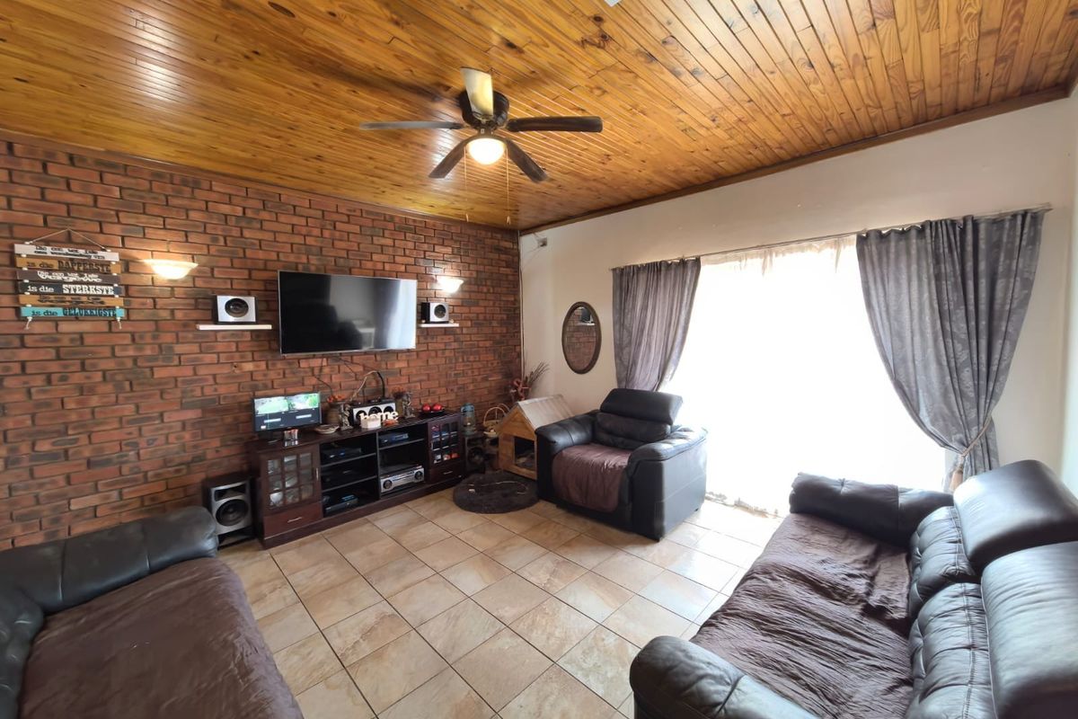 Living room featuring an exposed brick feature wall, timber ceiling, ceiling fan, and ceramic tiled flooring with access to the outdoors via sliding doors.