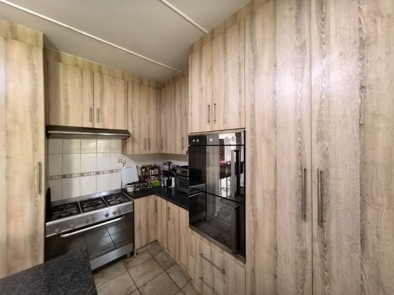 A functional kitchen featuring wood-look cabinetry, a built-in oven, gas hob, extractor fan, and tiled flooring with a neutral backsplash.