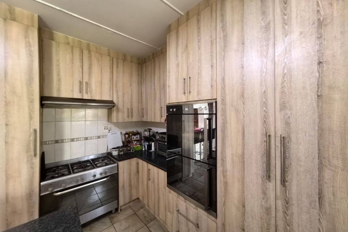 A functional kitchen featuring wood-look cabinetry, a built-in oven, gas hob, extractor fan, and tiled flooring with a neutral backsplash.