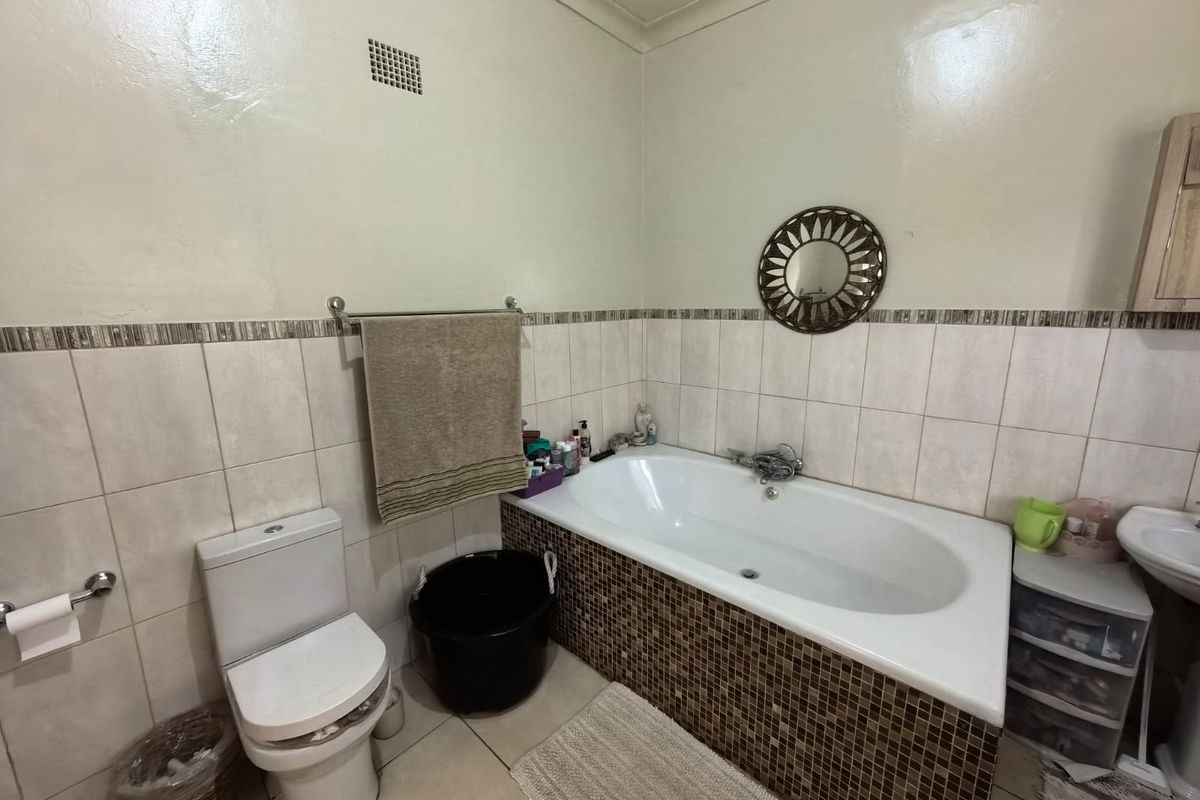 A functional bathroom featuring a built-in bathtub with mosaic tile surround, a standard toilet, and a pedestal basin with neutral wall tiling.