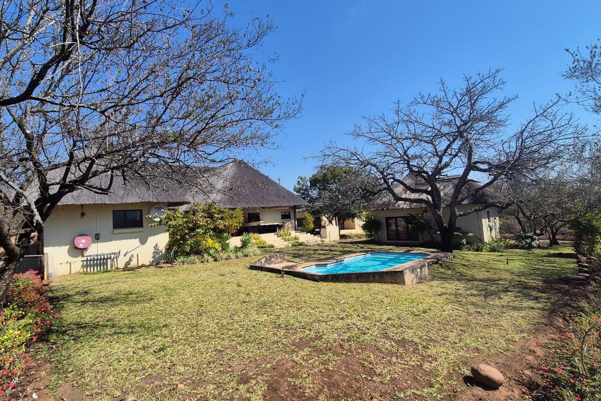 Rear view of the property featuring a thatched roof house, a swimming pool, and a spacious garden area.