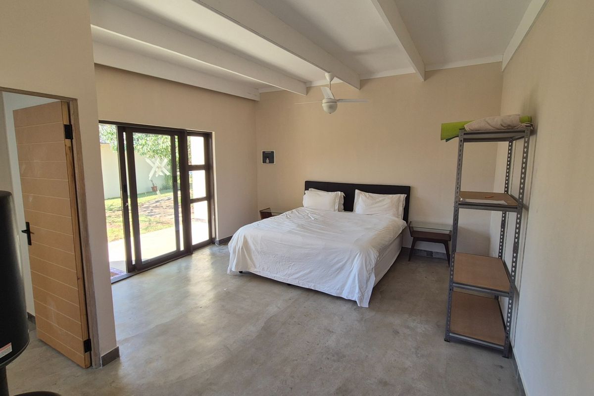 Spacious bedroom featuring exposed beam ceilings, polished concrete floors, and a large sliding glass door providing direct access to the garden.