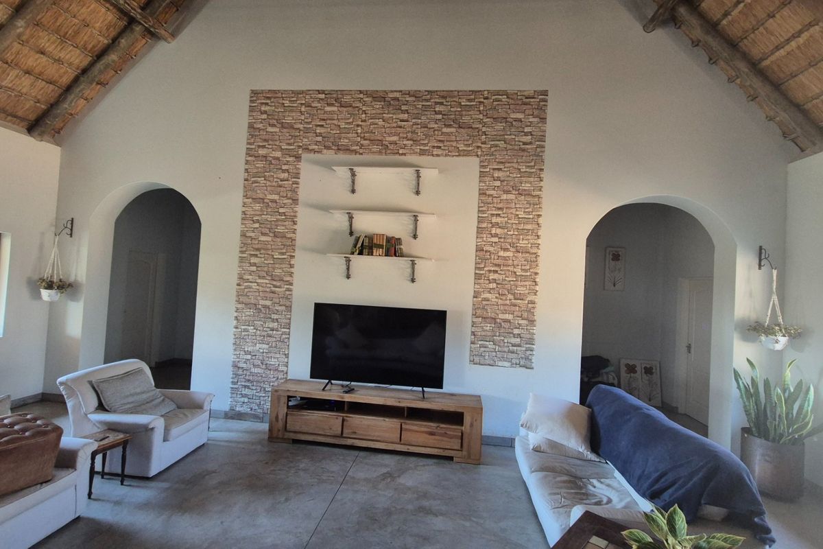 Spacious living room featuring a high vaulted thatched ceiling, polished concrete floors, and a stone-clad feature wall with built-in shelving.