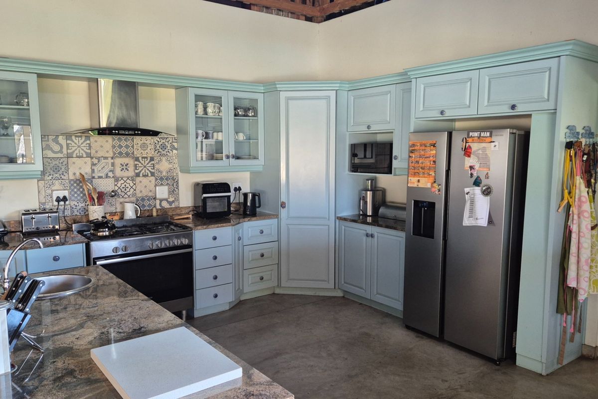 A well-appointed kitchen featuring light blue cabinetry, granite countertops, a gas stove with extractor fan, and a decorative tiled backsplash.