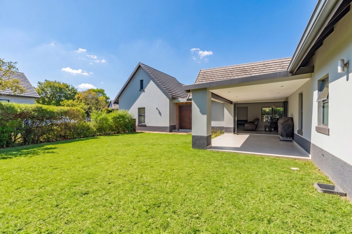 A well-maintained rear exterior view featuring a spacious lawn, a covered tiled patio, and modern architectural finishes with sliding door access to the interior.