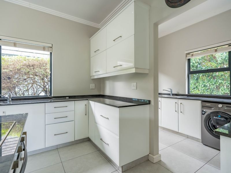Modern kitchen featuring white cabinetry, dark granite countertops, tiled flooring, and a separate scullery area with integrated laundry plumbing.