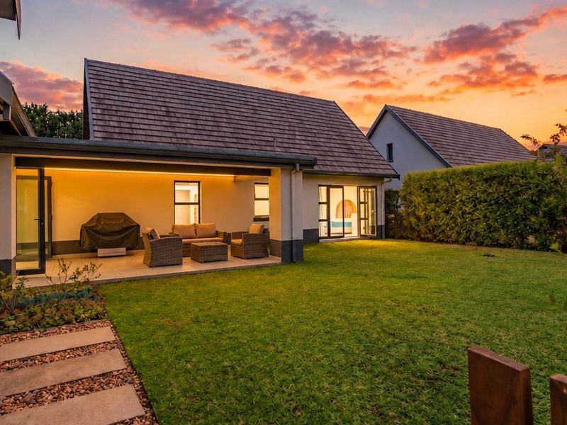 A well-maintained rear exterior featuring a covered patio with recessed lighting, sliding glass doors, and a landscaped garden at sunset.