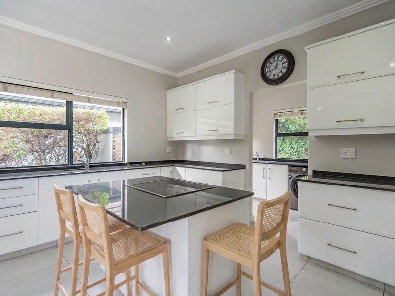 Modern kitchen featuring white cabinetry, granite countertops, a central island with a built-in hob, and a separate scullery area with laundry connections.
