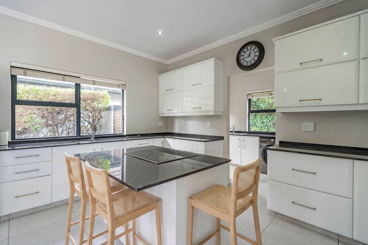 Modern kitchen featuring white cabinetry, granite countertops, a central island with a built-in hob, and a separate scullery area with laundry connections.