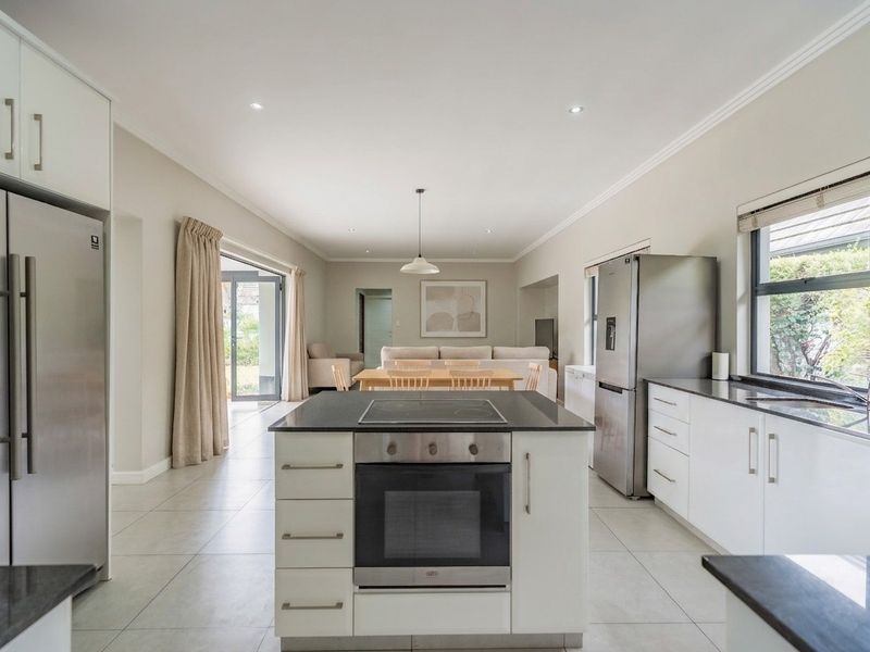 Spacious open-plan kitchen and living area featuring a central island with built-in oven, stone countertops, tiled floors, and seamless access to the outdoor patio.