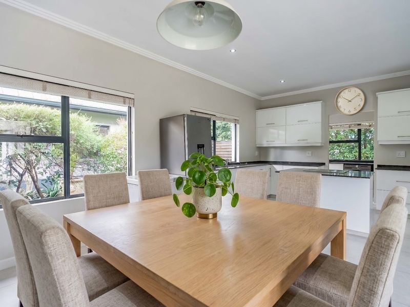 Bright open-plan kitchen and dining area featuring modern white cabinetry, granite countertops, tiled flooring, and large windows overlooking the garden.