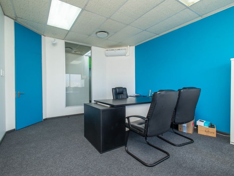 A professional office space featuring blue accent walls, carpeted flooring, a suspended ceiling with recessed lighting, and a wall-mounted air conditioning unit.