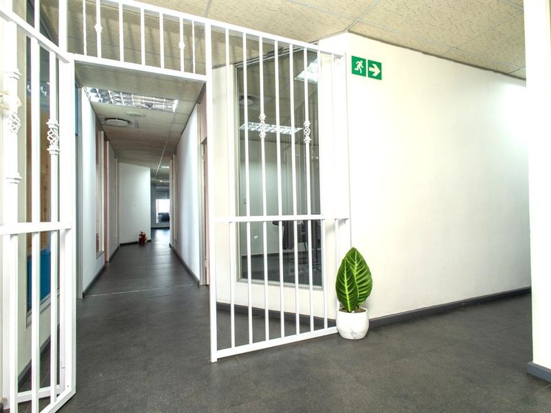 A functional office hallway featuring tiled flooring, a suspended ceiling with recessed lighting, and a white security gate at the entrance.