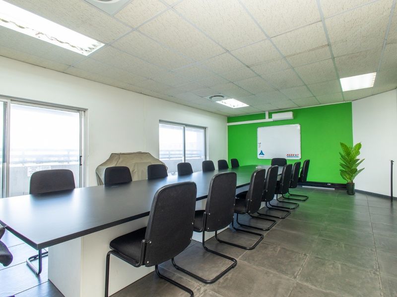 A functional office boardroom featuring tiled flooring, suspended ceiling with recessed lighting, air conditioning, and sliding glass doors providing natural light.
