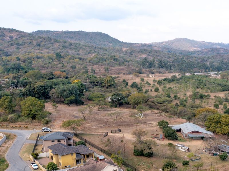 Aerial view of a large residential vacant land plot featuring natural vegetation, existing outbuildings, and surrounding neighborhood infrastructure.