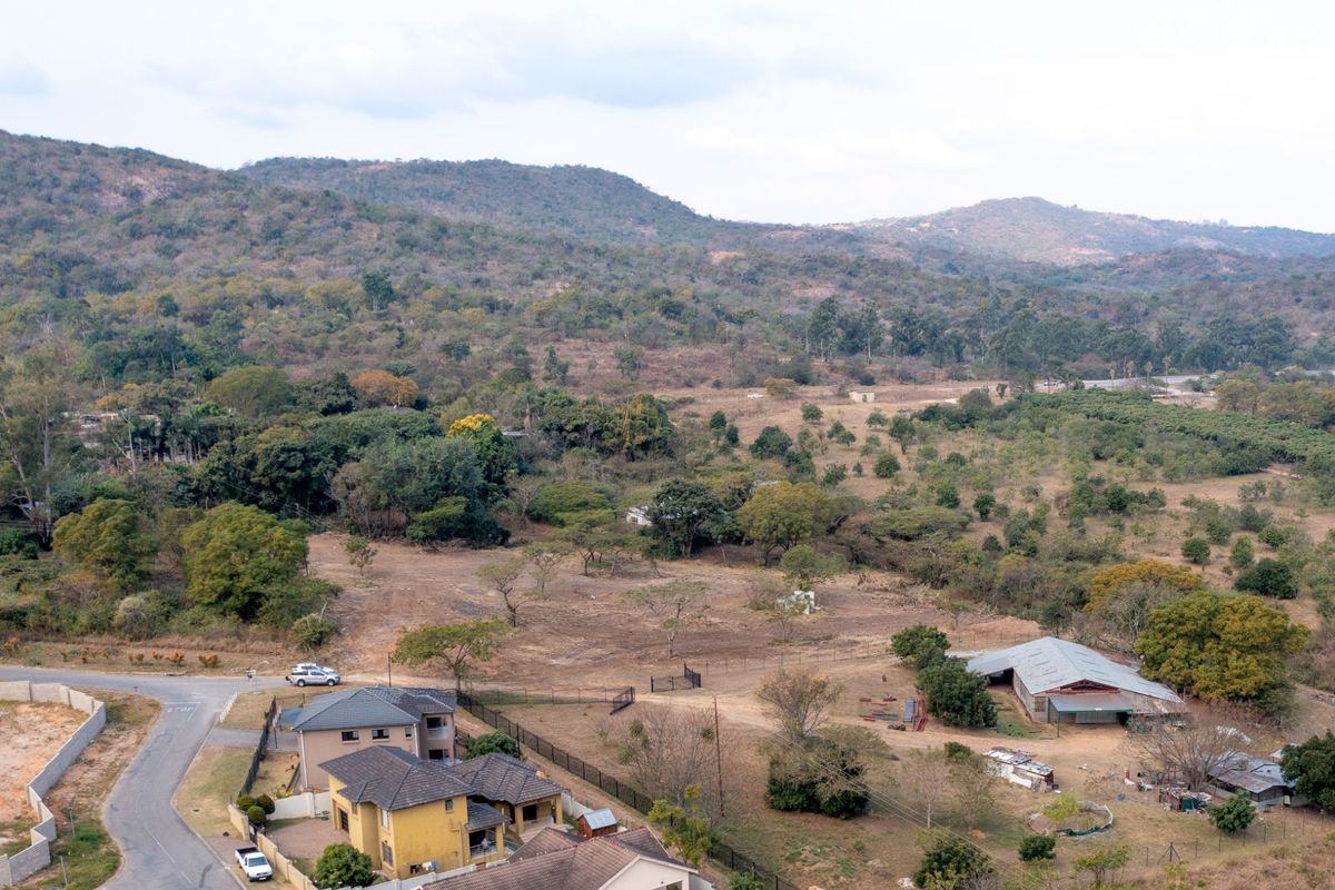 Aerial view of a large residential vacant land plot featuring natural vegetation, existing outbuildings, and surrounding neighborhood infrastructure.