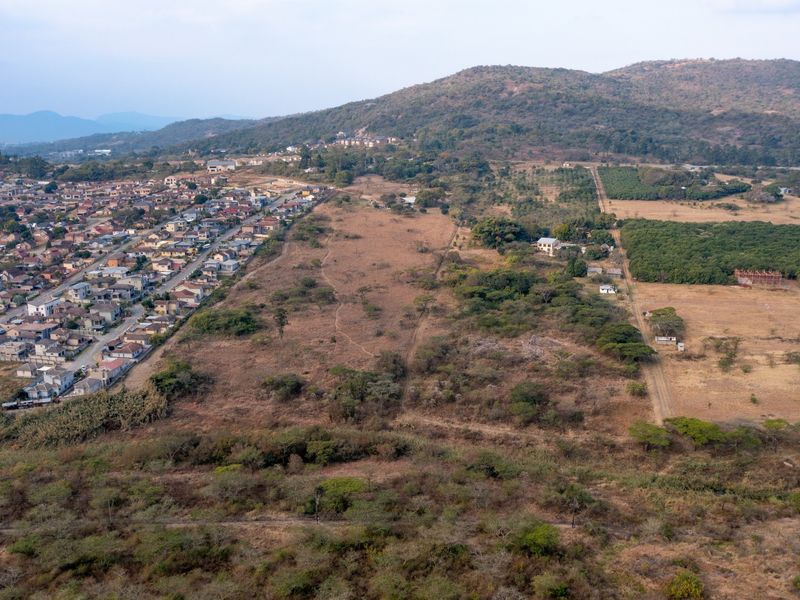 An aerial view of a large, undeveloped residential land parcel situated adjacent to an established suburban neighborhood and hilly landscape.