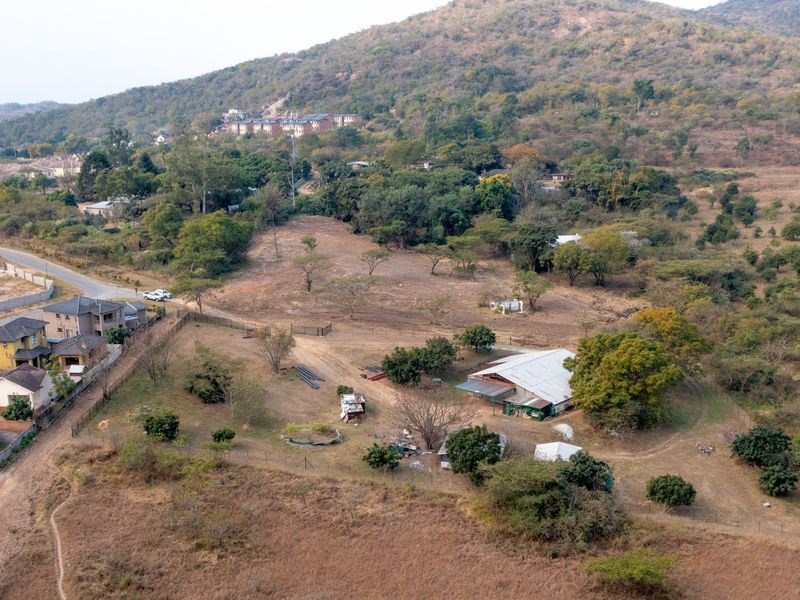 Aerial view of a large residential vacant land plot featuring established trees, fencing, and an existing structure on the property.