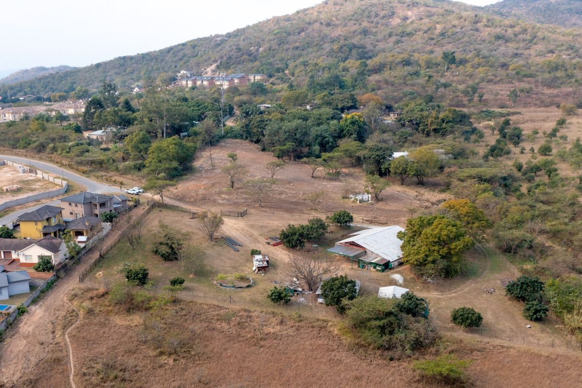 Aerial view of a large residential vacant land plot featuring established trees, fencing, and an existing structure on the property.