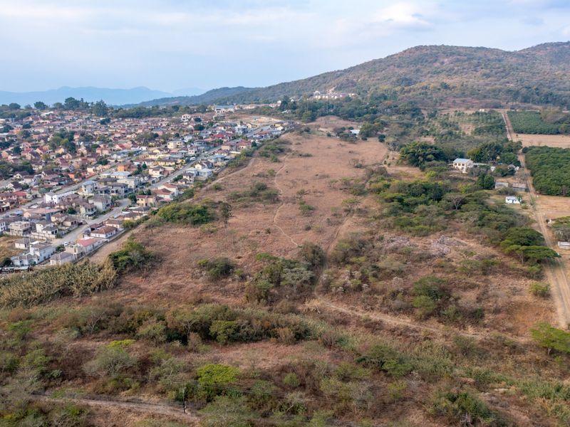 An aerial view showing the surrounding landscape, nearby residential development, and open terrain adjacent to the property.
