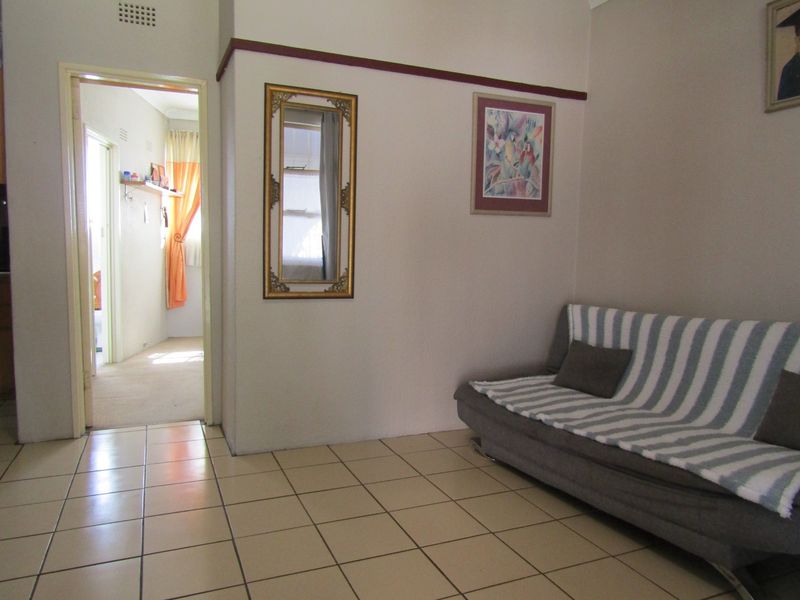 A living area featuring neutral ceramic floor tiles and a traditional picture rail, providing a functional space with access to an adjoining room.