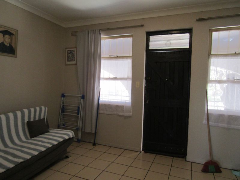 A living area featuring tiled flooring, a dark security door, and dual windows with curtains, providing a functional space with potential for modernization.
