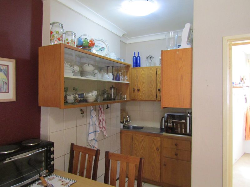 A compact kitchen area featuring dated wooden cabinetry, tiled splashbacks, and a stainless steel sink, offering functional storage and preparation space.