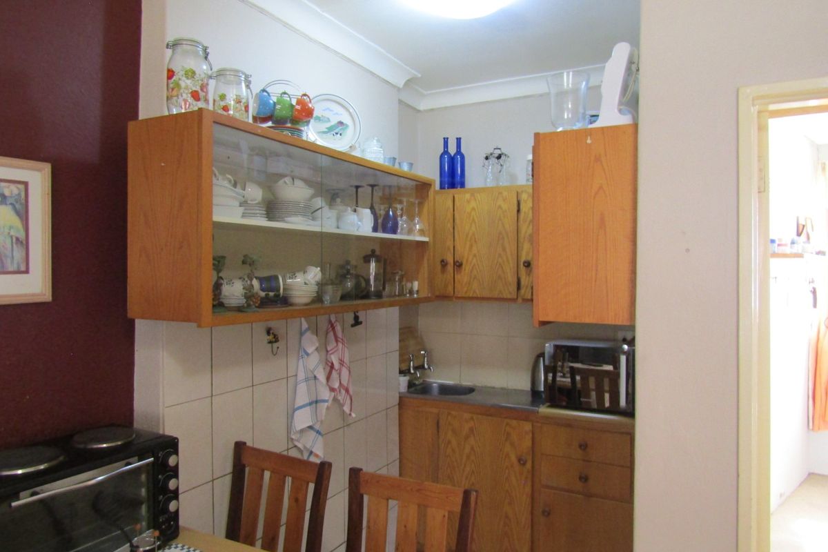 A compact kitchen area featuring dated wooden cabinetry, tiled splashbacks, and a stainless steel sink, offering functional storage and preparation space.