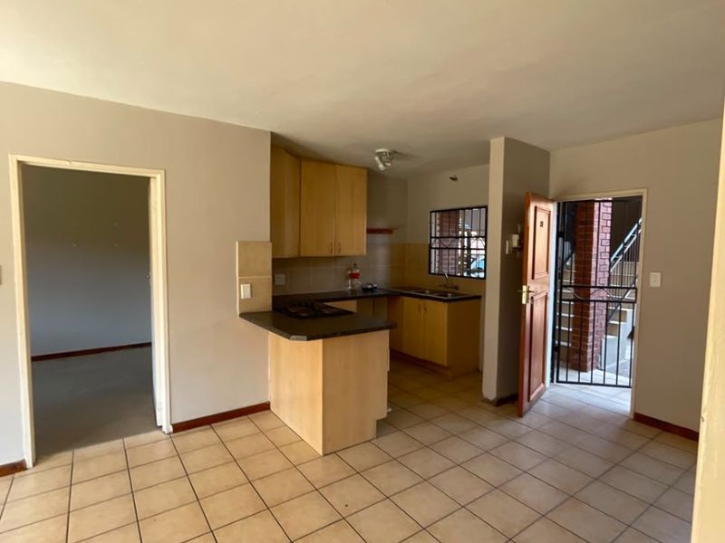 Open-plan kitchen and living area featuring ceramic tiled flooring, built-in cabinetry, and direct access to an exterior entrance with a security gate.