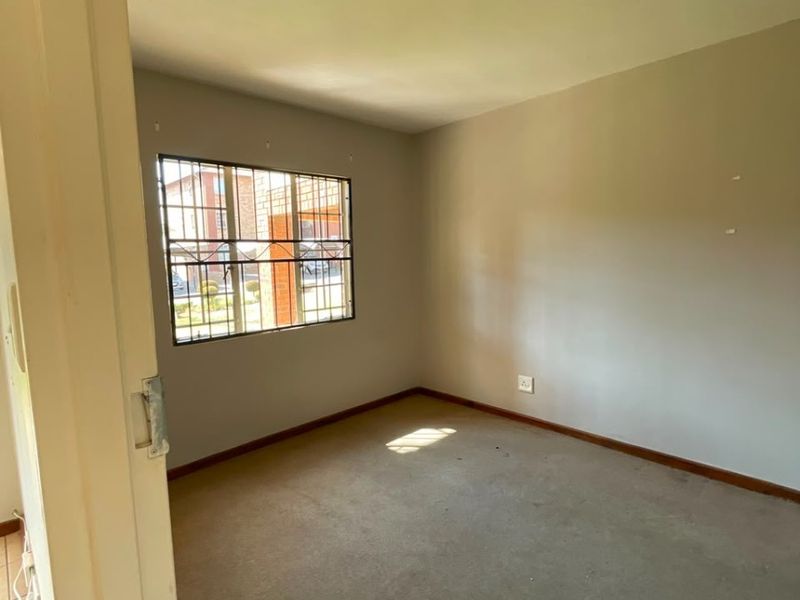 An empty bedroom featuring carpet flooring, neutral walls, and a window fitted with security bars.