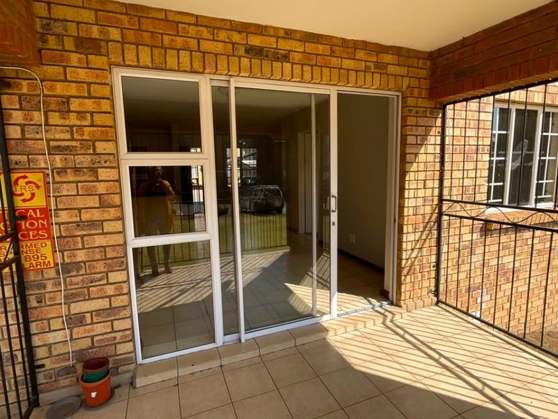 A covered patio area featuring tiled flooring, exposed brick walls, and a sliding glass door providing access to the interior living space.
