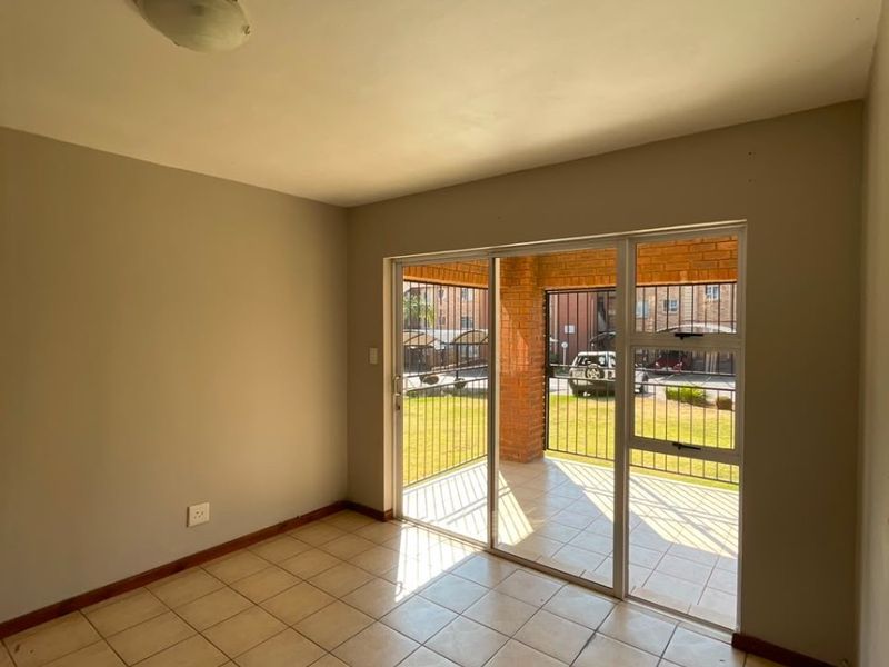 An empty living room featuring neutral tiled flooring and a large sliding glass door providing access to a covered patio area.