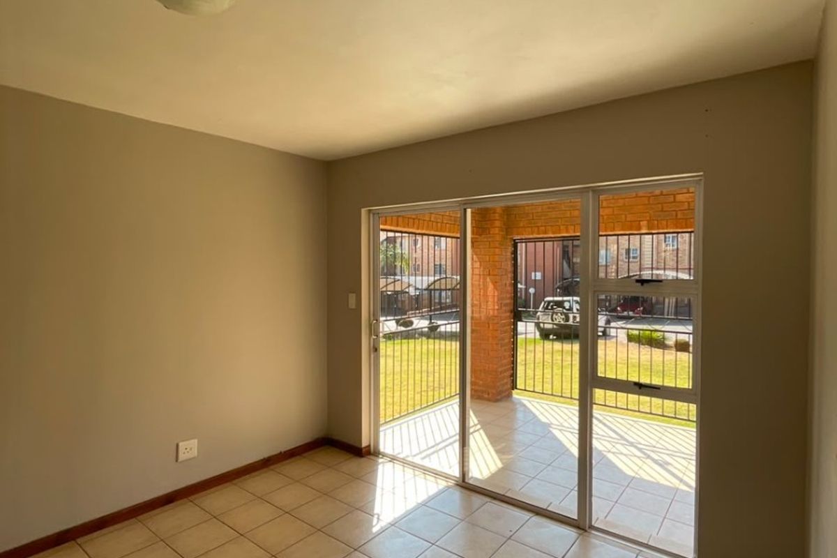 An empty living room featuring neutral tiled flooring and a large sliding glass door providing access to a covered patio area.