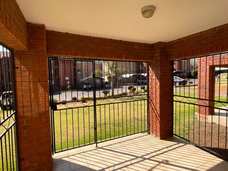 A covered patio area featuring brick pillars, tiled flooring, and secure metal gate enclosures, overlooking the complex grounds.