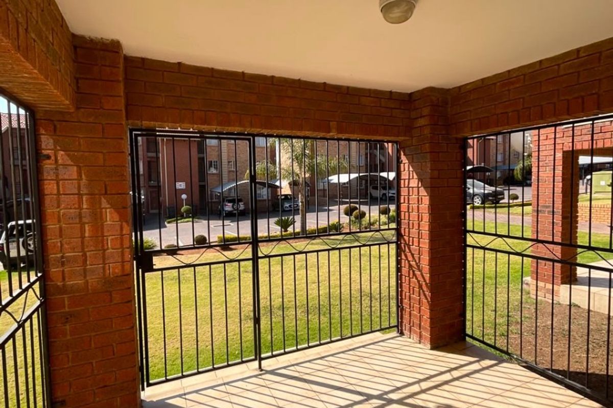 A covered patio area featuring brick pillars, tiled flooring, and secure metal gate enclosures, overlooking the complex grounds.