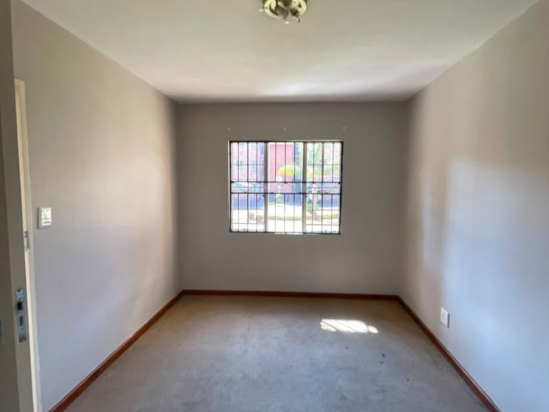 An empty bedroom featuring neutral walls, carpet flooring, and a window fitted with security bars.