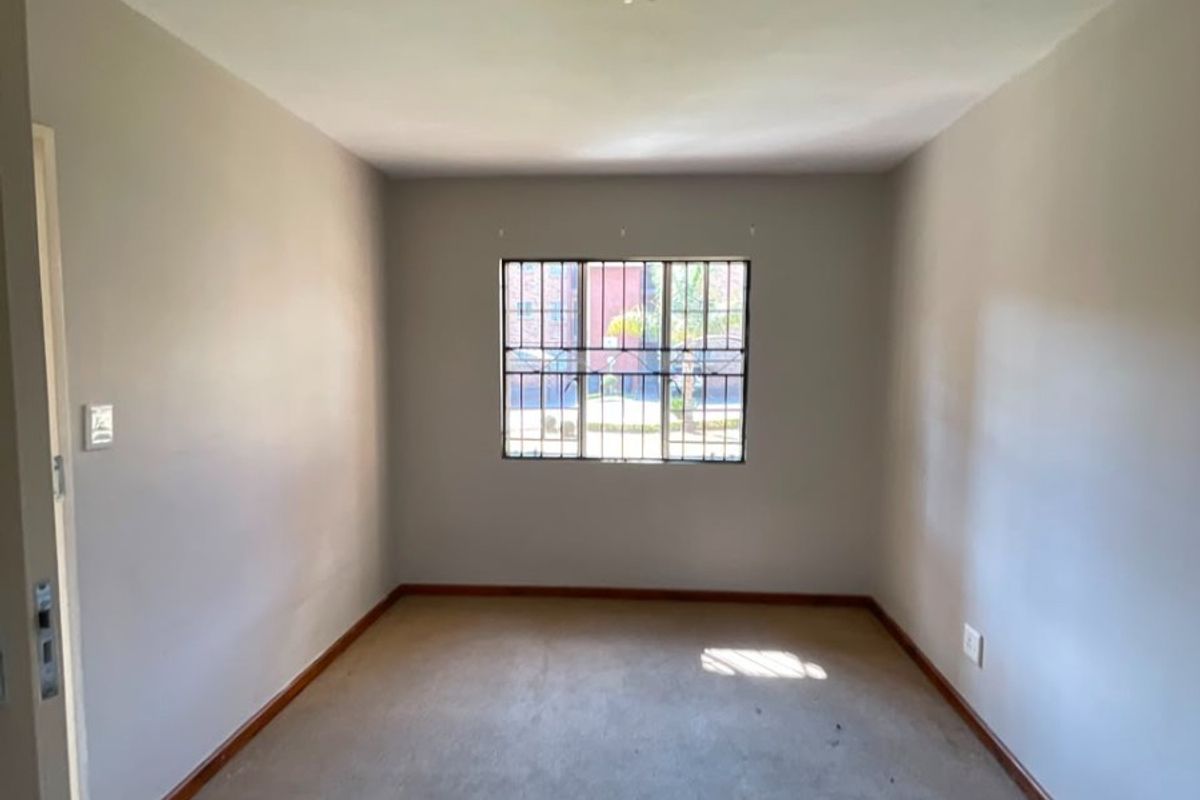 An empty bedroom featuring neutral walls, carpet flooring, and a window fitted with security bars.