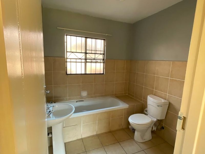 A functional bathroom featuring a pedestal basin, built-in bathtub, and toilet with neutral wall and floor tiling.