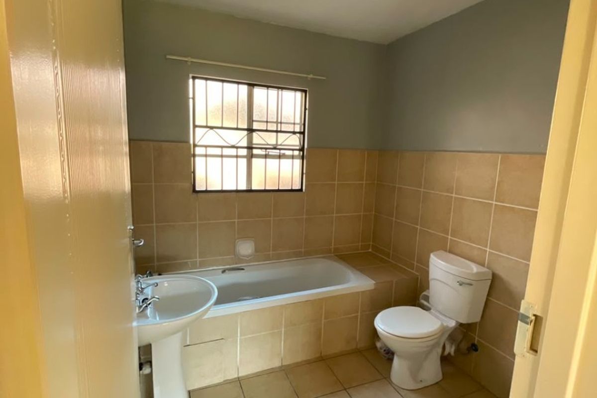A functional bathroom featuring a pedestal basin, built-in bathtub, and toilet with neutral wall and floor tiling.