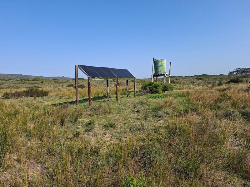 Outdoor utility area featuring a ground-mounted solar panel array and an elevated water storage tank on a timber frame structure.