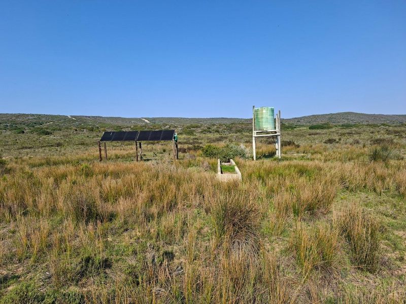 Open farm land featuring a solar panel array, a raised water storage tank, and a concrete livestock water trough.
