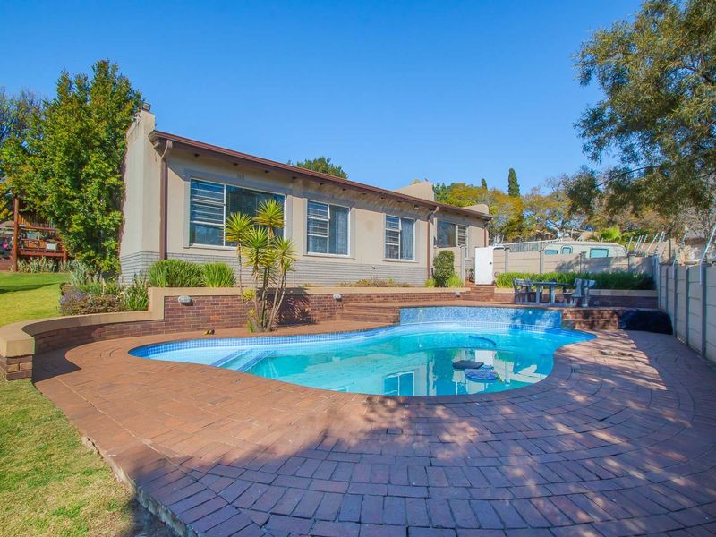 Rear garden area featuring a swimming pool, brick paved patio, and tiered retaining walls, set against the rear elevation of the house.
