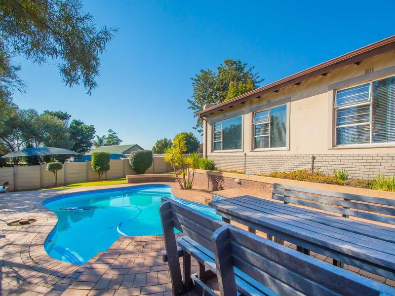 Outdoor pool area featuring a swimming pool, brick paved surround, and a retaining wall, set against a private garden with boundary walling.