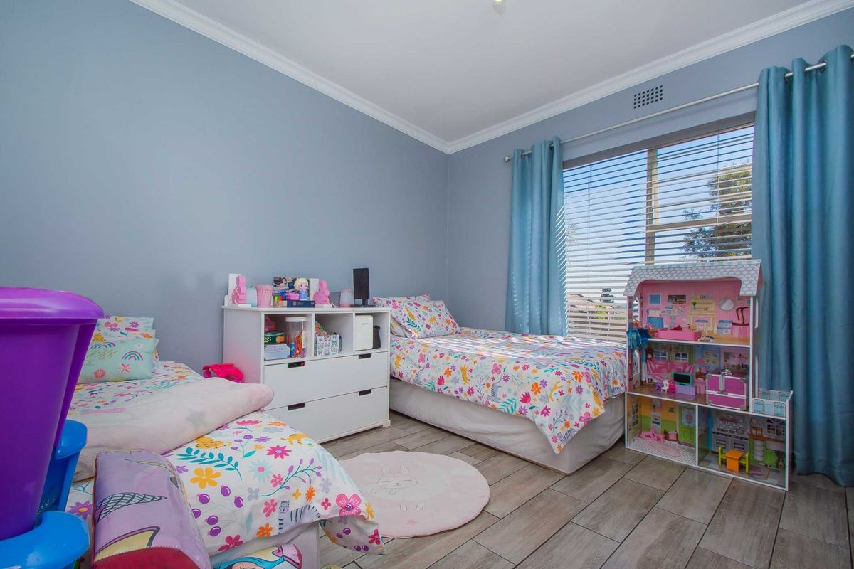 A well-maintained bedroom featuring tiled flooring, neutral wall paint, and large windows with fitted blinds, providing a bright and functional living space.
