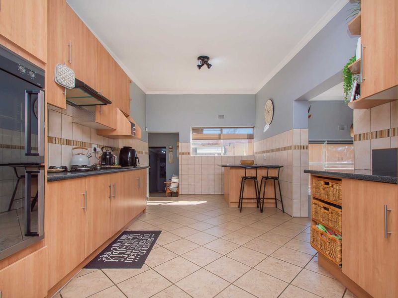 A functional kitchen featuring light wood cabinetry, tiled splashbacks, built-in oven, hob, and a breakfast nook area with tiled flooring throughout.