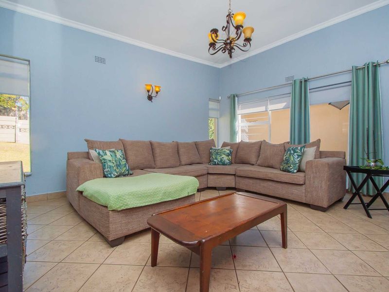 A spacious living room featuring ceramic tile flooring, decorative wall sconces, a classic chandelier, and sliding glass doors providing access to the exterior.