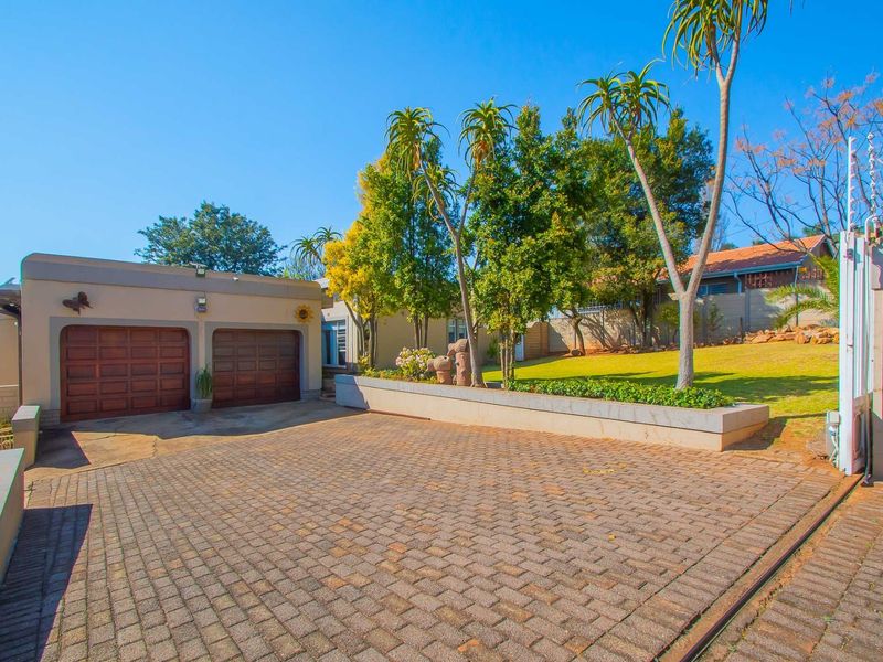 Front exterior view featuring a paved driveway, double garage, landscaped garden with retaining wall, and secure perimeter fencing.