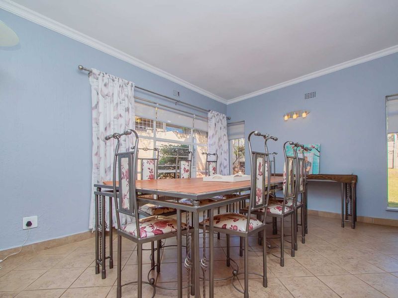A bright dining room featuring tiled flooring, coved cornicing, and large windows that provide natural light and views of the garden.
